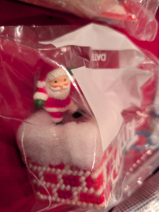 A packaged product featuring a plastic canvas design of Santa Claus coming out of a chimney, with red and white colors predominately visible.