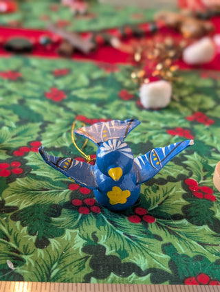 Blue decorative bird ornament on a green fabric background with red berries